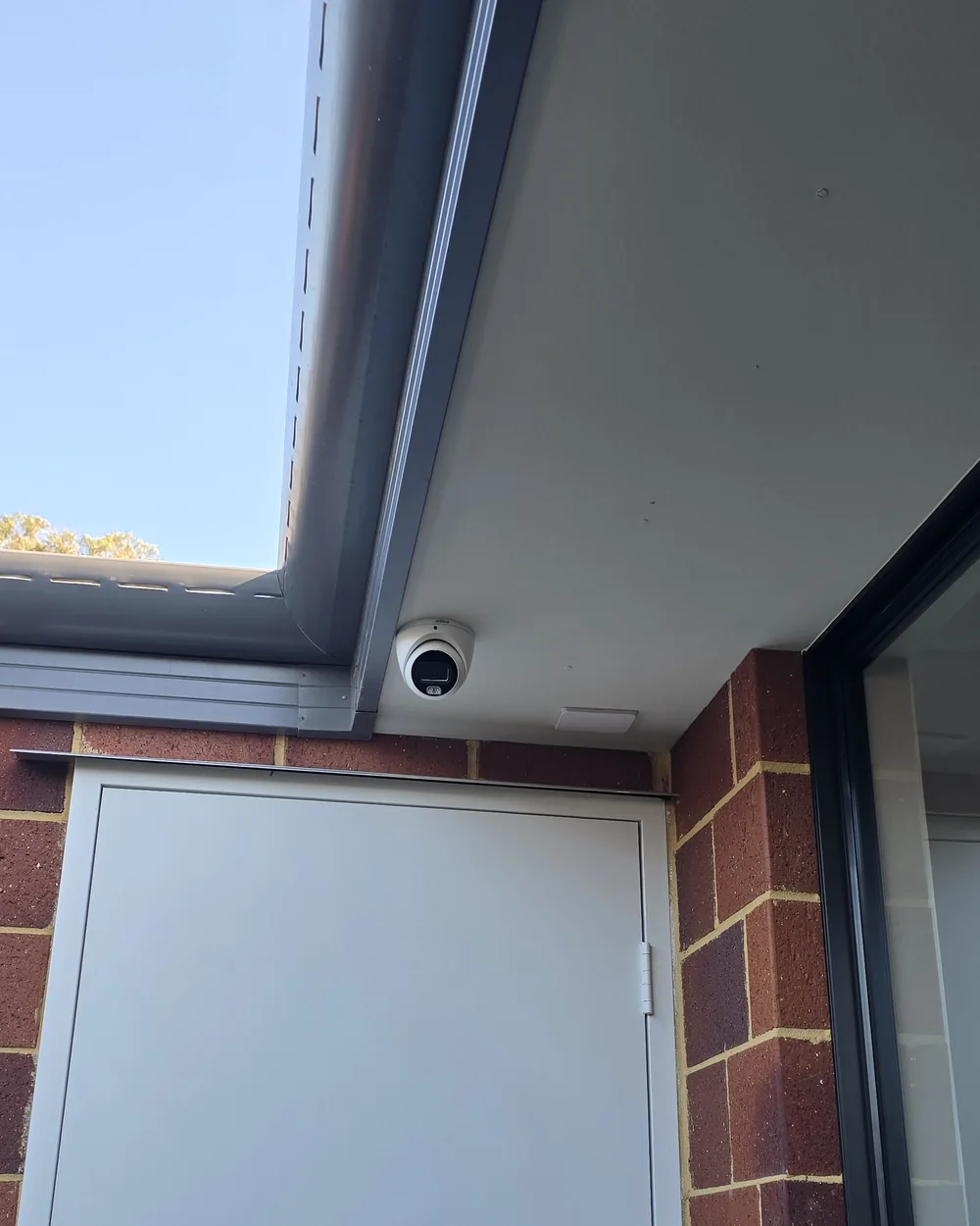 Camera moved forward from the exterior wall Dahua turret camera under the eave near a side entry door on a brick home