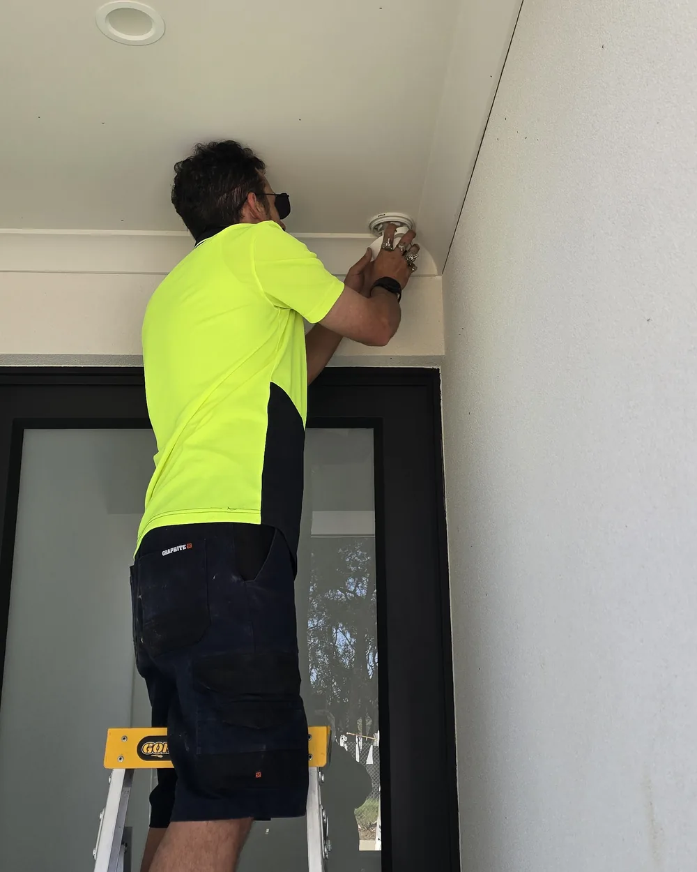 Installer fitting the camera under the eave CCTV installer on a ladder fitting a Dahua camera into the eave above an entry door