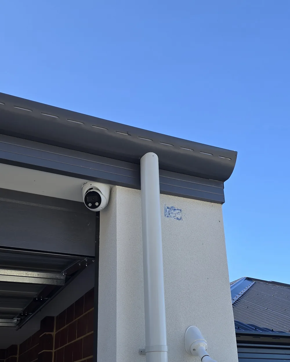 Dahua camera beside the garage downpipe Dahua turret camera mounted under the eave beside a white downpipe on a rendered garage wall